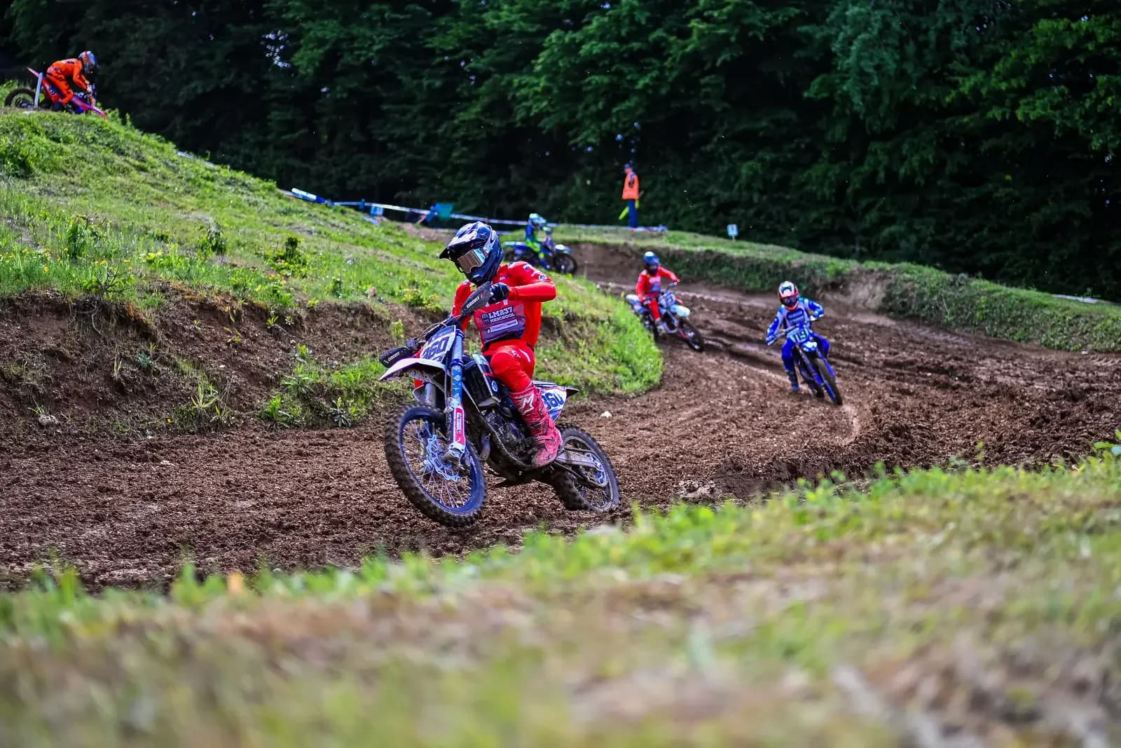 Motokrosisti v ovinku blatne proge, za njimi gozd