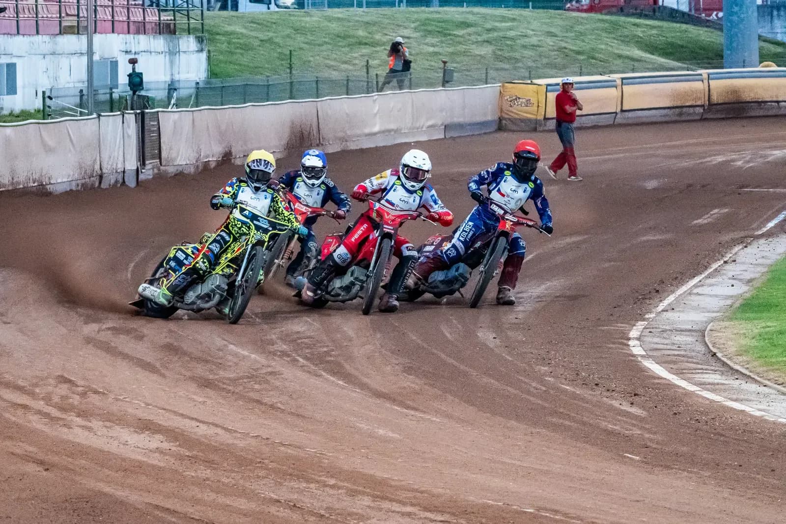 Four speedway riders side by side in a bend on a sand track